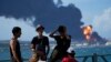 Jóvenes observan la columna de humo que se eleva del sitio de la catástrofe, en la zona industrial de Matanzas. Las autoridades advierten del peligro de contaminación. (AP/Ramon Espinosa).