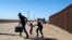 Una familia de migrantes de Cuba cruza corriendo la frontera por el muro que separa a Estados Unidos y México para entregarse a las autoridades el 13 de mayo de 2021 en Yuma, Arizona. (Foto de RINGO CHIU / AFP)